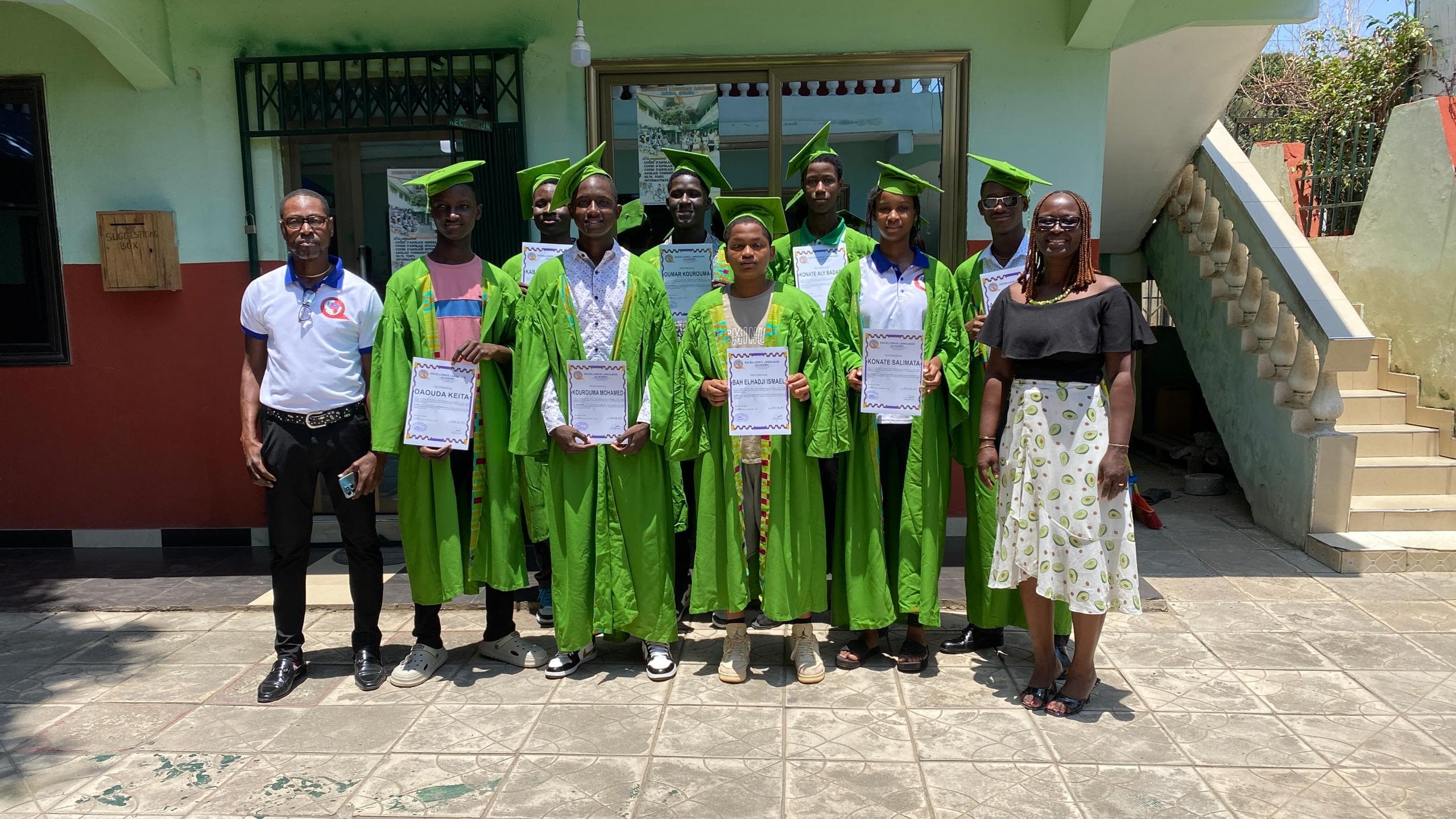 ELA graduates holding their certificates in front of the school